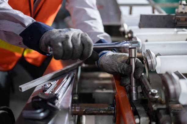 Close-up of a factory worker using a wrench to adjust machinery, showcasing industrial maintenance and precision work.