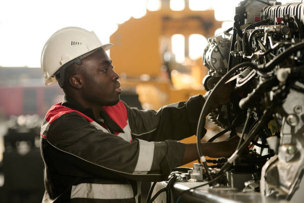 Side view of young male engineer in workwear checking hydraulic hoses and other details of indistrial machine while working in factory