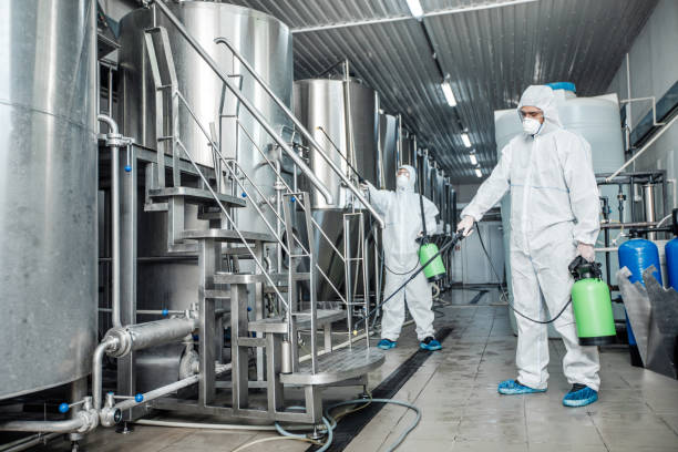 Professional disinfection of equipment during quarantine. Guys in protective suits and glasses works in interior of plant, free space